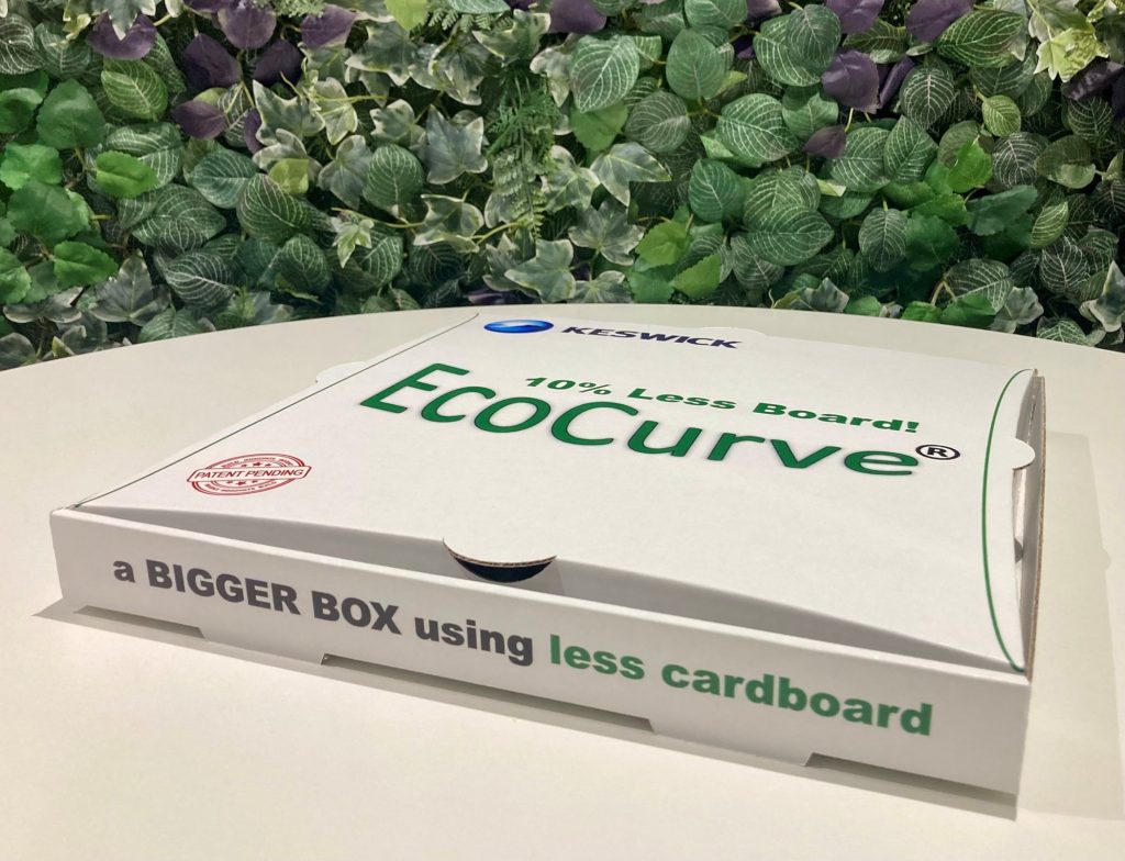 White EcoCurve pizza box with curved sides displayed on a table against a green foliage background.