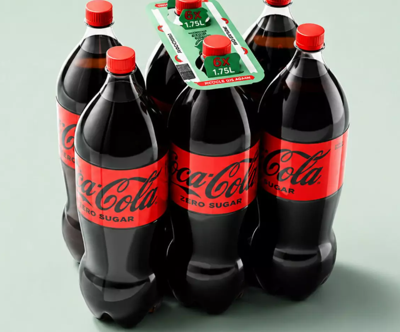 Four Coca-Cola PET bottles grouped together with a cardboard carrying handle attached across the bottle tops.