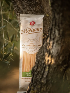 La Molisana spaghetti pack standing beside an olive tree, featuring cream-coloured branding, a transparent pasta window and green compostability messaging.